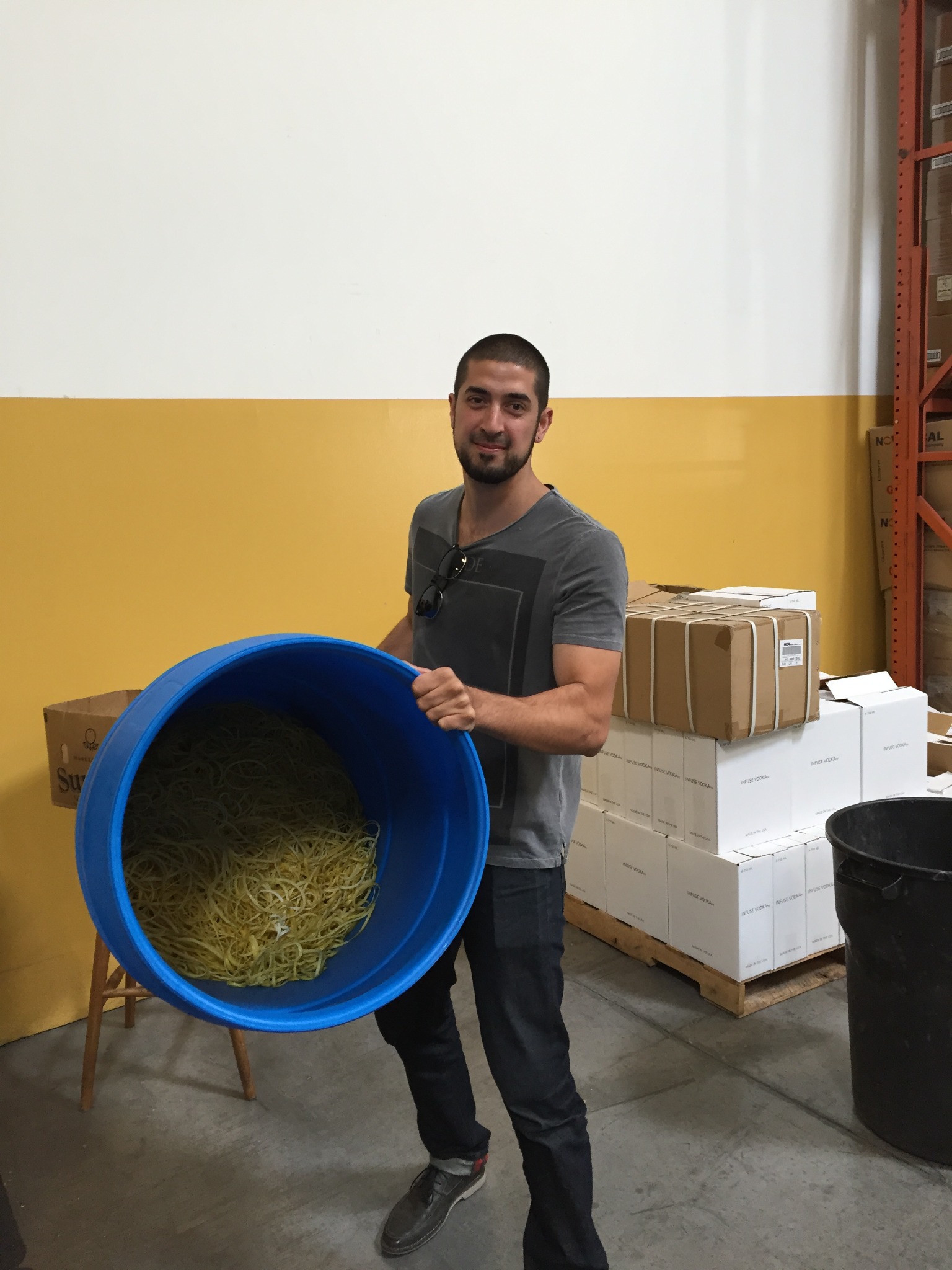 Seth holding a blue barrel of lemon peels beside Infuse Spirits boxes