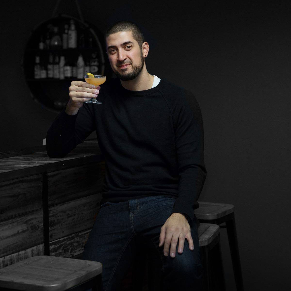 Seth Benhaim seated at a bar raising a cocktail